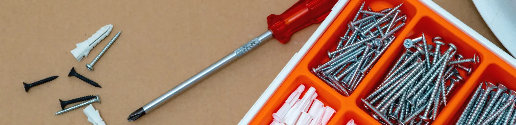 Skruvmejsel med rött handtag och låda med skruv och plugg