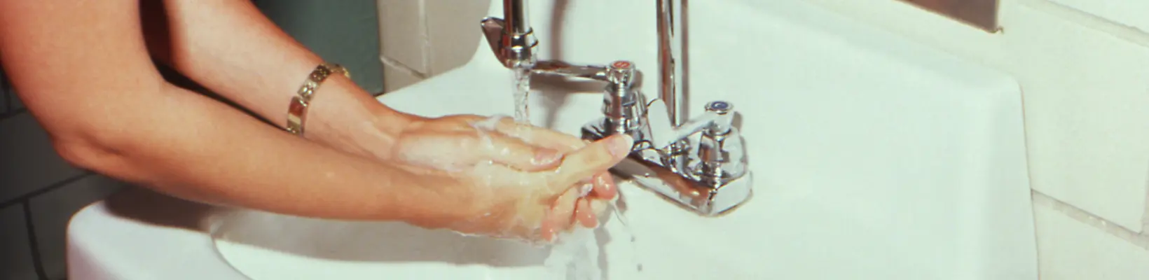 Person som tvättar händerna med vatten som rinner ur en kran vattenlås